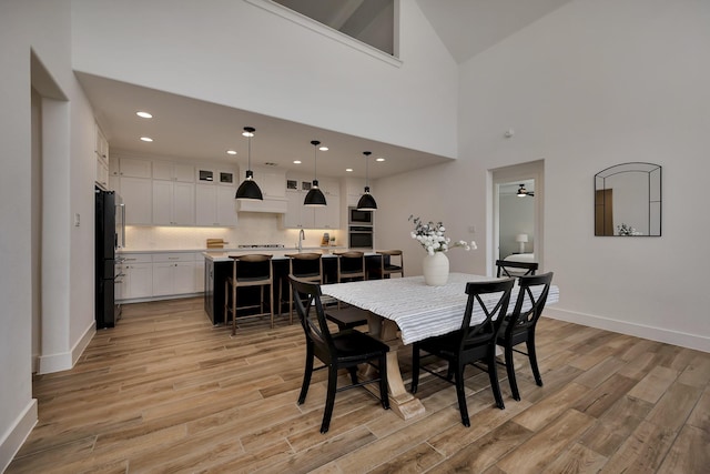 dining room with a high ceiling, recessed lighting, light wood-style floors, and baseboards