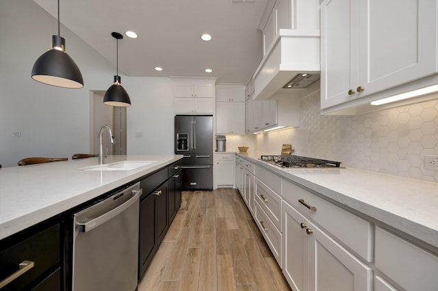 kitchen featuring appliances with stainless steel finishes, light wood-style floors, custom exhaust hood, white cabinetry, and a sink