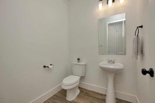 half bathroom with toilet, wood finished floors, baseboards, and a sink