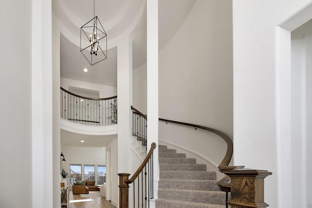 staircase with an inviting chandelier, wood finished floors, and a towering ceiling