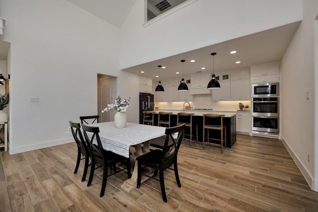 dining room with recessed lighting, baseboards, a towering ceiling, and light wood finished floors