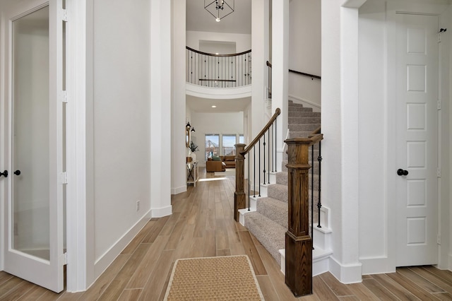 foyer entrance featuring a high ceiling, stairs, light wood-type flooring, and baseboards