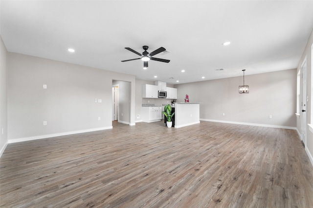 unfurnished living room with light wood-style flooring, ceiling fan with notable chandelier, and baseboards