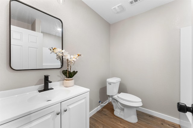 half bathroom with visible vents, baseboards, toilet, wood finished floors, and vanity