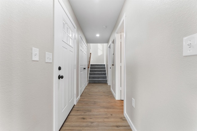 corridor with a textured wall, stairway, baseboards, and wood finished floors