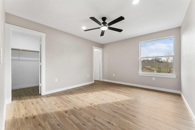 unfurnished bedroom with recessed lighting, a walk in closet, baseboards, and light wood-style floors