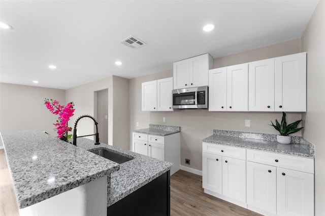 kitchen with visible vents, a kitchen island with sink, a sink, stainless steel microwave, and light stone countertops