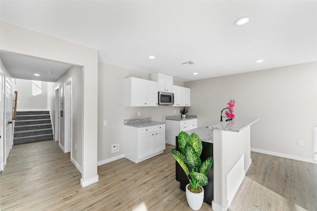 kitchen featuring stainless steel microwave, light wood-style floors, visible vents, and light stone countertops