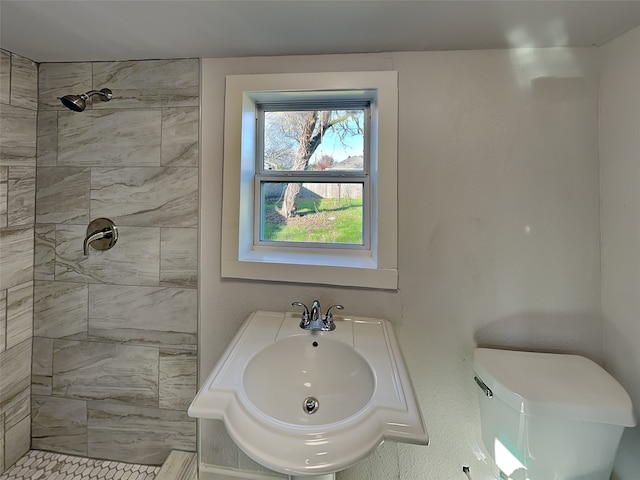 full bath with toilet, a tile shower, and a sink