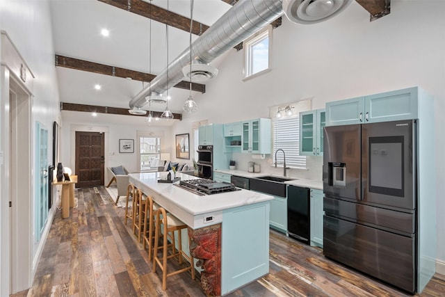 kitchen featuring a high ceiling, a sink, light countertops, appliances with stainless steel finishes, and blue cabinets