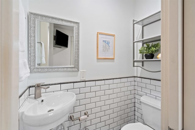 bathroom featuring tile walls, toilet, a wainscoted wall, and a sink