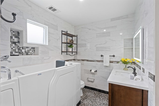 full bathroom featuring visible vents, tile walls, toilet, a bath, and vanity