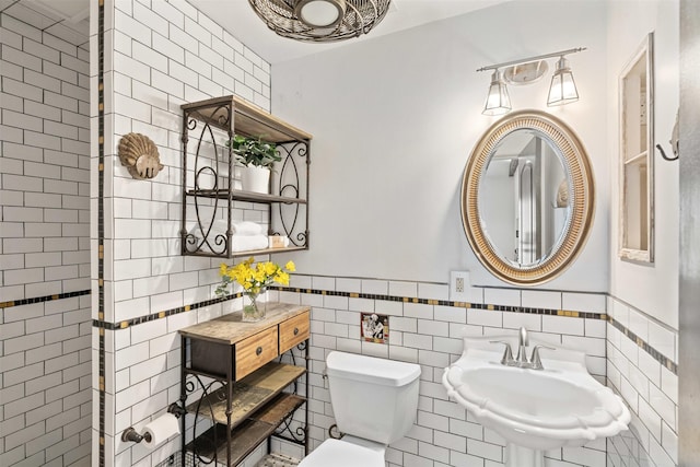 bathroom with a sink, toilet, tile walls, and wainscoting