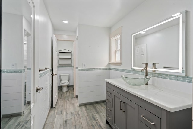 full bathroom featuring vanity, wood finished floors, wainscoting, tile walls, and toilet