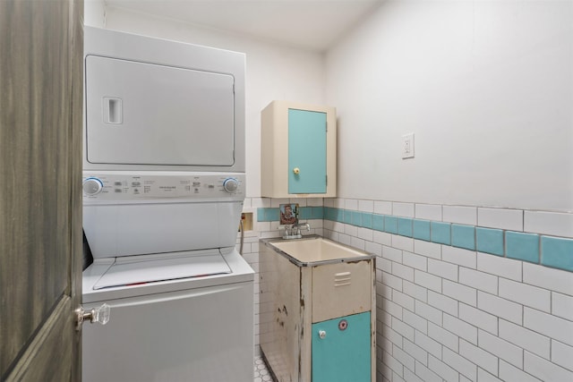 laundry room with a wainscoted wall, stacked washer and dryer, tile walls, and laundry area