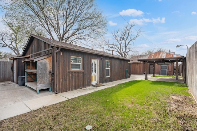 rear view of property with board and batten siding, central AC unit, a yard, a fenced backyard, and a patio area