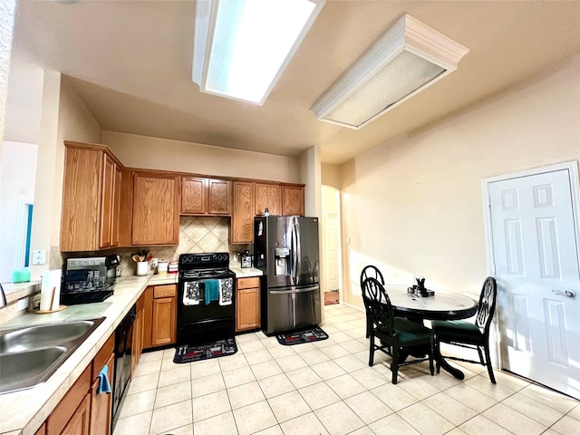 kitchen featuring brown cabinetry, a sink, black appliances, light countertops, and tasteful backsplash