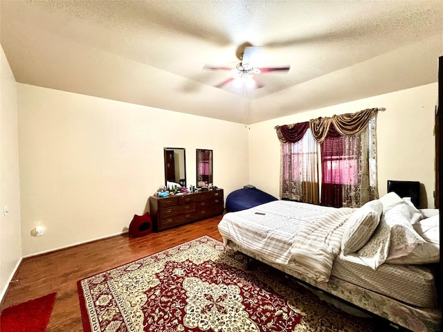 bedroom featuring ceiling fan, baseboards, a textured ceiling, and wood finished floors