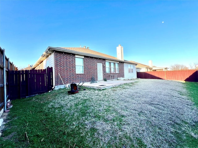 rear view of property featuring a lawn, a fenced backyard, brick siding, a chimney, and a patio area