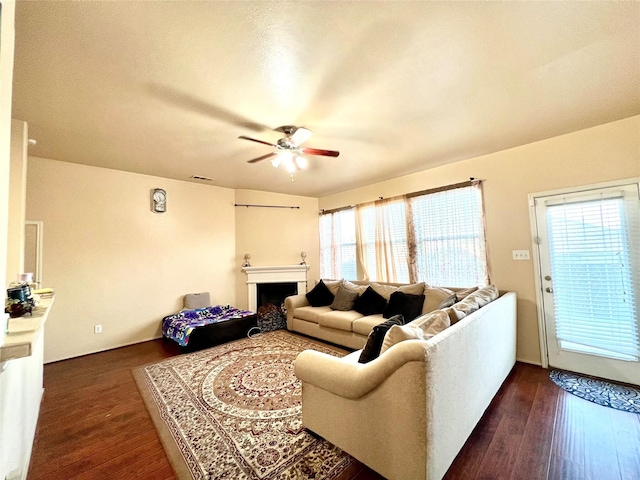 living room with a fireplace, dark wood-type flooring, and a ceiling fan