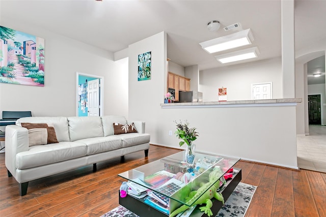 living area with arched walkways, visible vents, lofted ceiling, and hardwood / wood-style floors