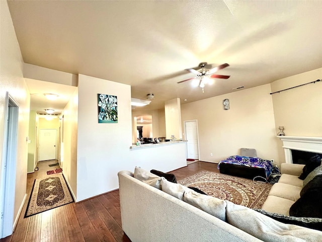 living room with visible vents, dark wood-type flooring, ceiling fan, and a fireplace