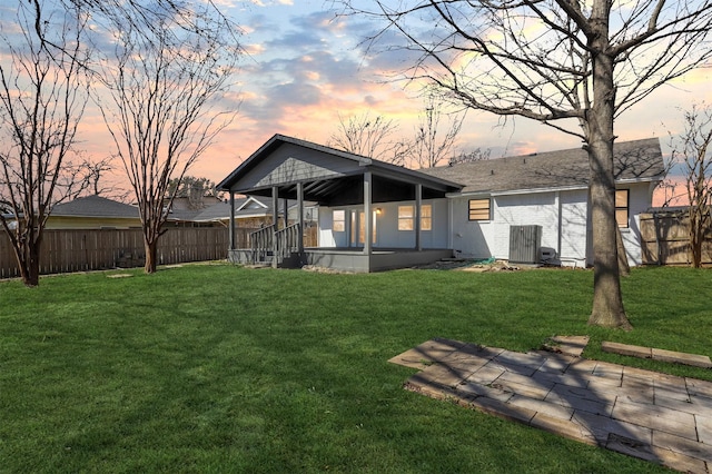 back of property at dusk with a yard, a porch, fence, and central AC