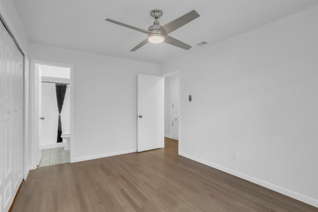 unfurnished bedroom with ensuite bath, visible vents, baseboards, and wood finished floors