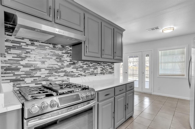 kitchen featuring tasteful backsplash, gray cabinets, under cabinet range hood, visible vents, and stainless steel range with gas cooktop
