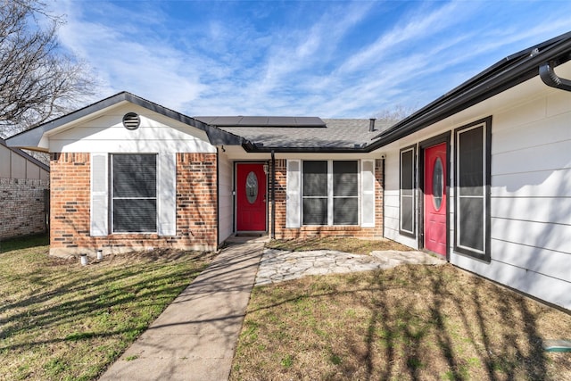 doorway to property featuring brick siding, roof mounted solar panels, and a lawn