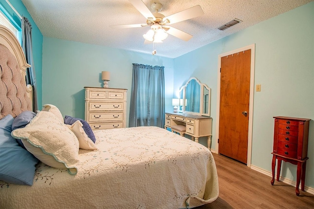 bedroom with visible vents, a textured ceiling, wood finished floors, baseboards, and ceiling fan