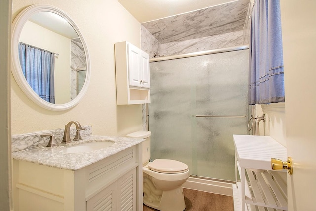 bathroom with a shower stall, toilet, vanity, and wood finished floors