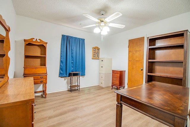 unfurnished office featuring a ceiling fan, light wood-style floors, and a textured ceiling