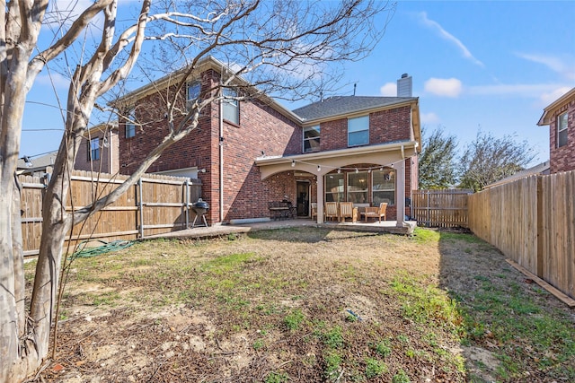 rear view of house featuring brick siding, a lawn, a chimney, a fenced backyard, and a patio area