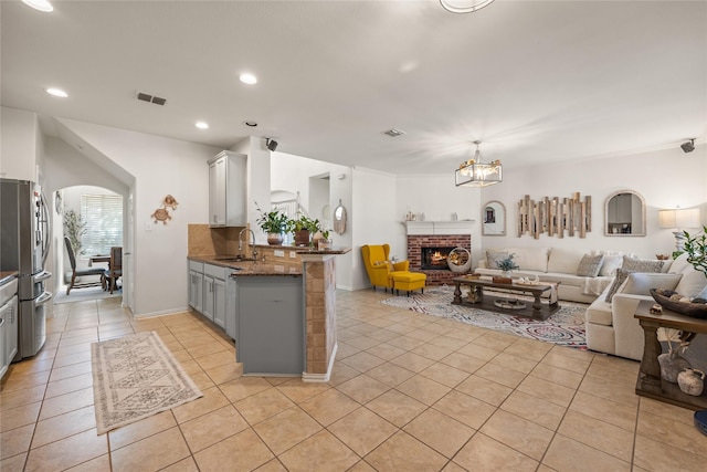 kitchen featuring a peninsula, light tile patterned flooring, freestanding refrigerator, a sink, and open floor plan