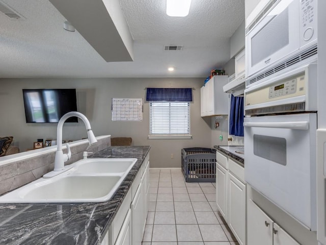 kitchen featuring dark countertops, visible vents, light tile patterned floors, white oven, and a sink