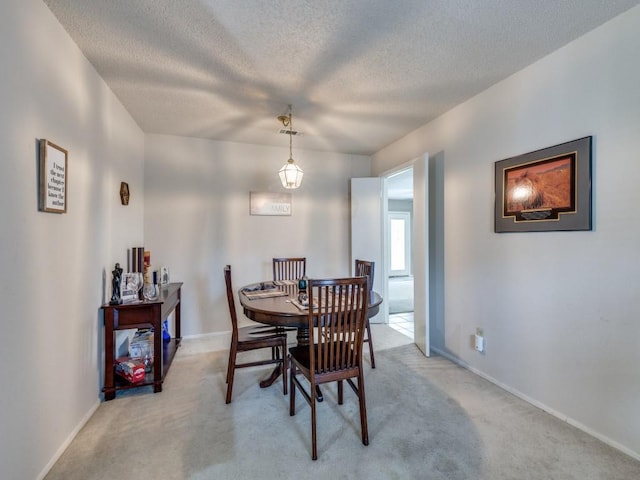 dining space featuring light colored carpet, a textured ceiling, and baseboards