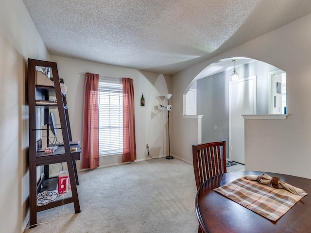 dining space with baseboards, carpet, arched walkways, and a textured ceiling