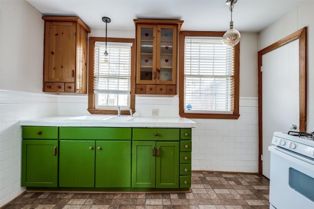kitchen featuring tile walls, decorative light fixtures, white range with gas stovetop, and a wainscoted wall