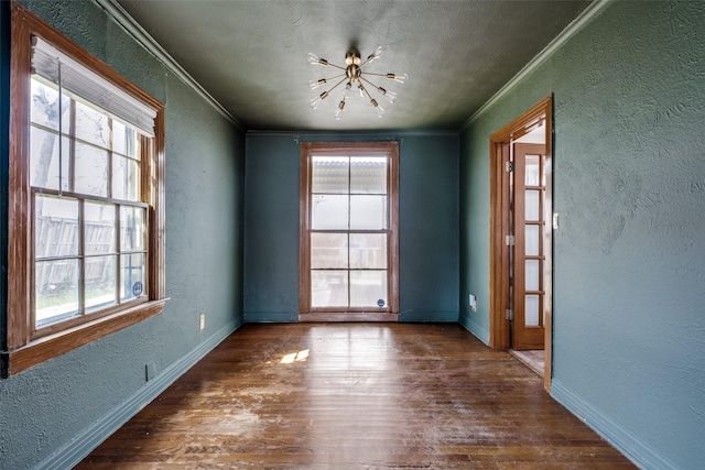 unfurnished room featuring wood finished floors, a notable chandelier, a textured wall, and ornamental molding