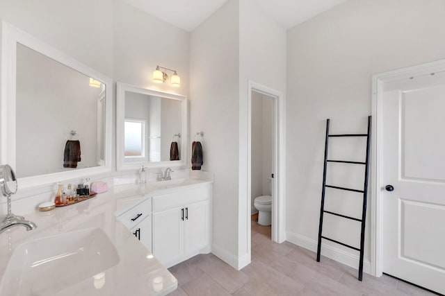 bathroom with double vanity, toilet, baseboards, and a sink