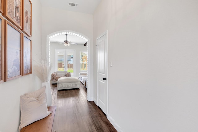 hallway with arched walkways, visible vents, baseboards, and dark wood-style floors