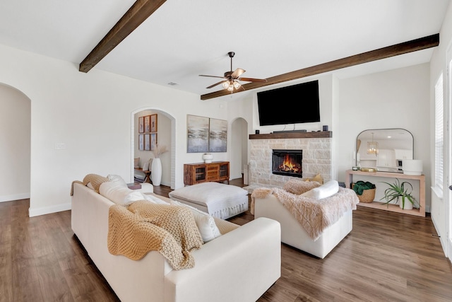 living area featuring arched walkways, a stone fireplace, beamed ceiling, and ceiling fan