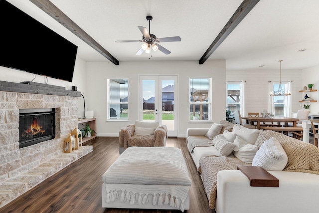 living room with baseboards, a stone fireplace, dark wood-type flooring, beamed ceiling, and ceiling fan with notable chandelier