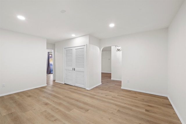 spare room with arched walkways, recessed lighting, light wood-style flooring, and baseboards