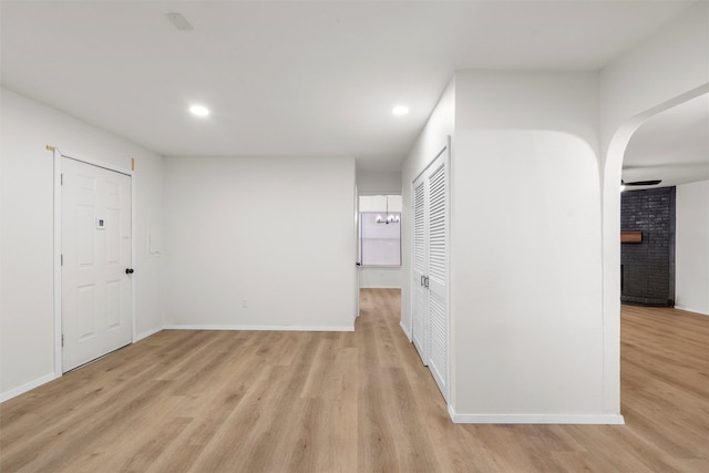 interior space featuring light wood-type flooring, recessed lighting, arched walkways, a fireplace, and baseboards