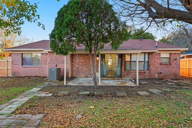 rear view of house with a patio, central AC unit, fence, a shingled roof, and brick siding