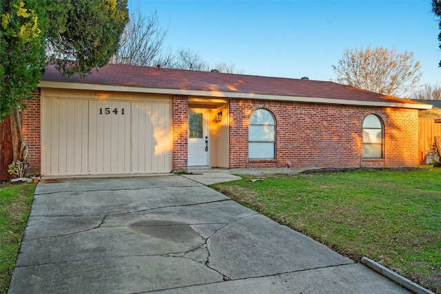 ranch-style house with a front yard, driveway, an attached garage, a shingled roof, and brick siding
