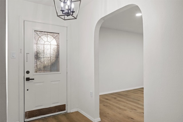 foyer entrance with arched walkways, a notable chandelier, baseboards, and wood finished floors