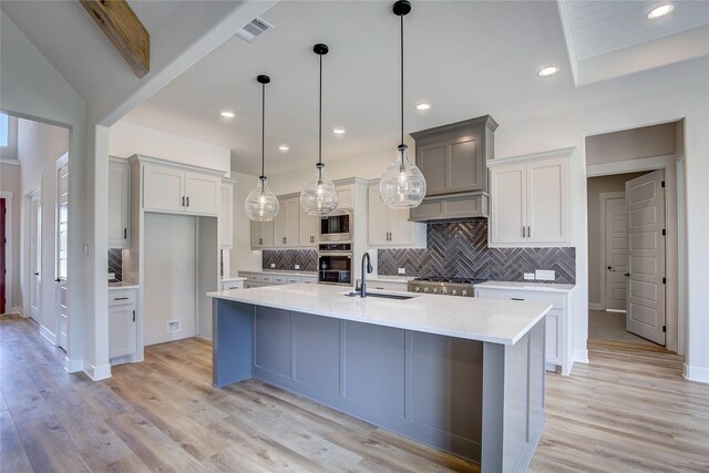 kitchen featuring visible vents, light wood finished floors, stainless steel microwave, a sink, and an island with sink